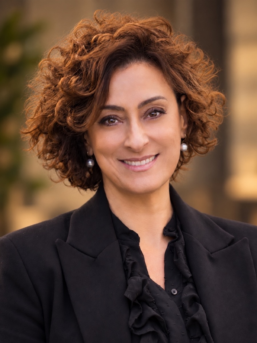Portrait of Cinzia Perlingieri, smiling, with short curly auburn hair, wearing a black blazer
